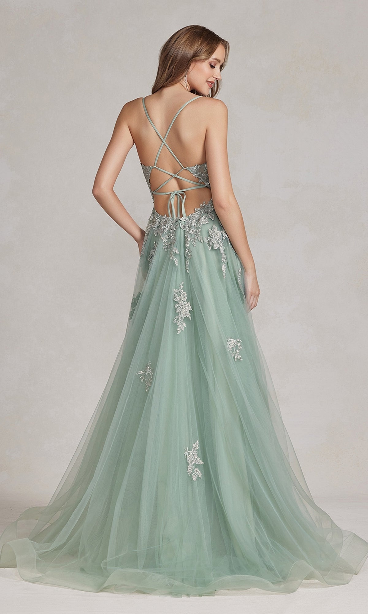 A woman in an Open-Back Long Prom Ball Gown with Beads, featuring light green fabric, floor-length a-line silhouette, beaded lace appliques, and a lace-up open back, stands facing away.